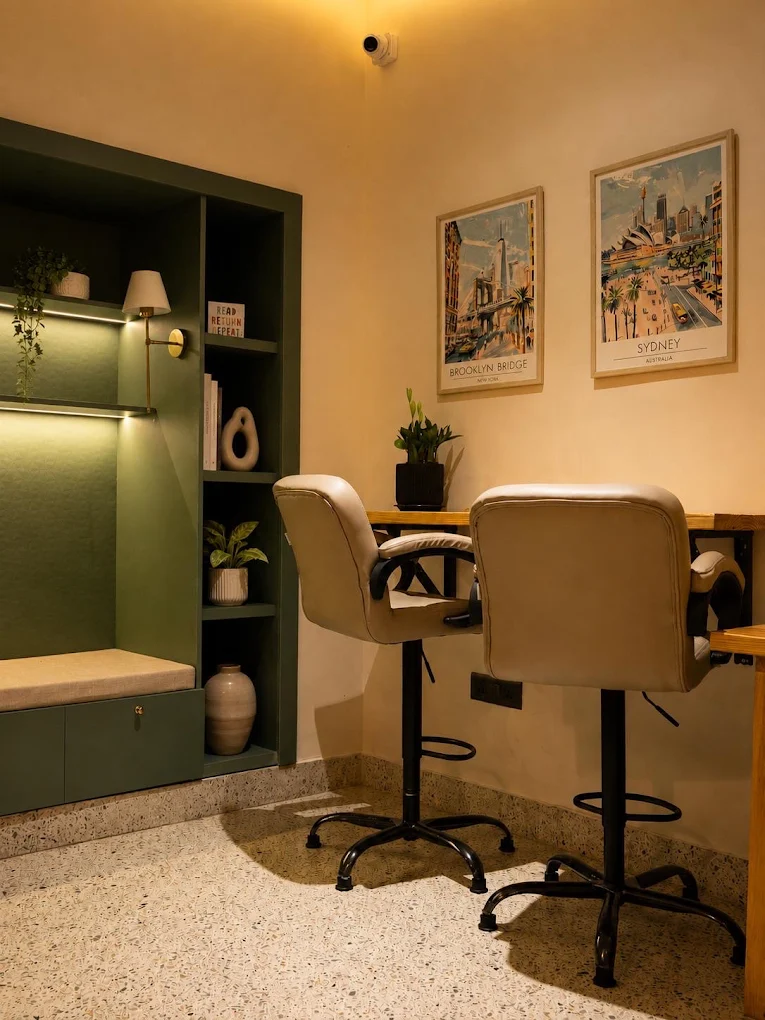 A warm cowork nook with two high chairs, a wooden desk and a sage green bookshelf