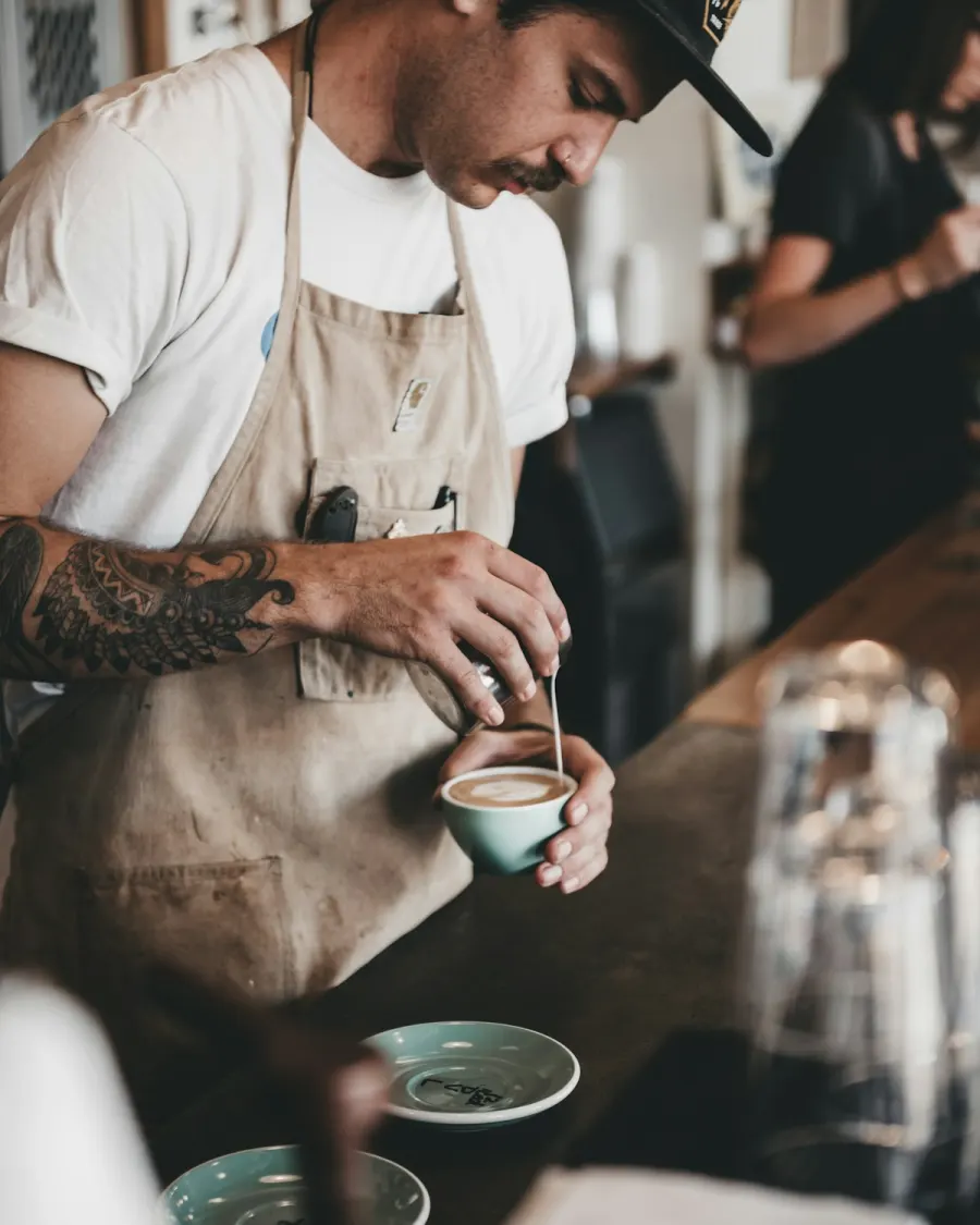 A barista pouring steamed milk into a cup of coffee