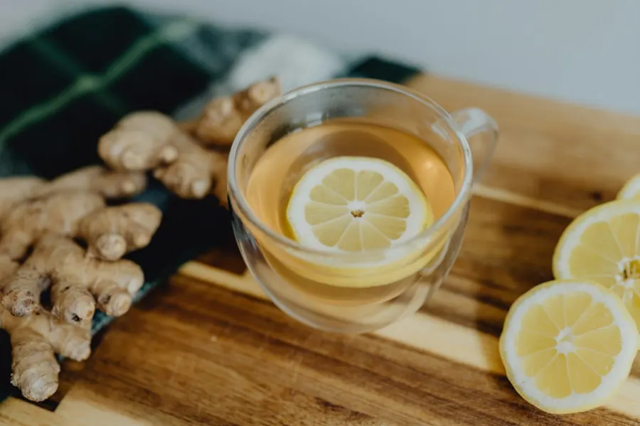 A glass cup of ginger and lemon tea on a wooden board