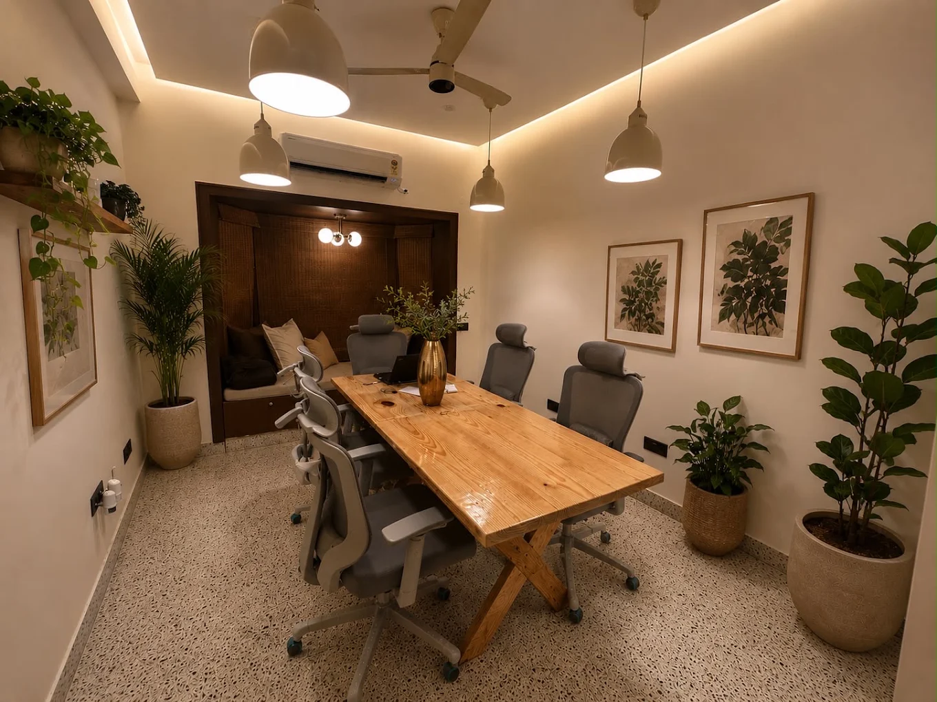 A meeting room with a long wooden table, pendant lamps, botanical prints and plants